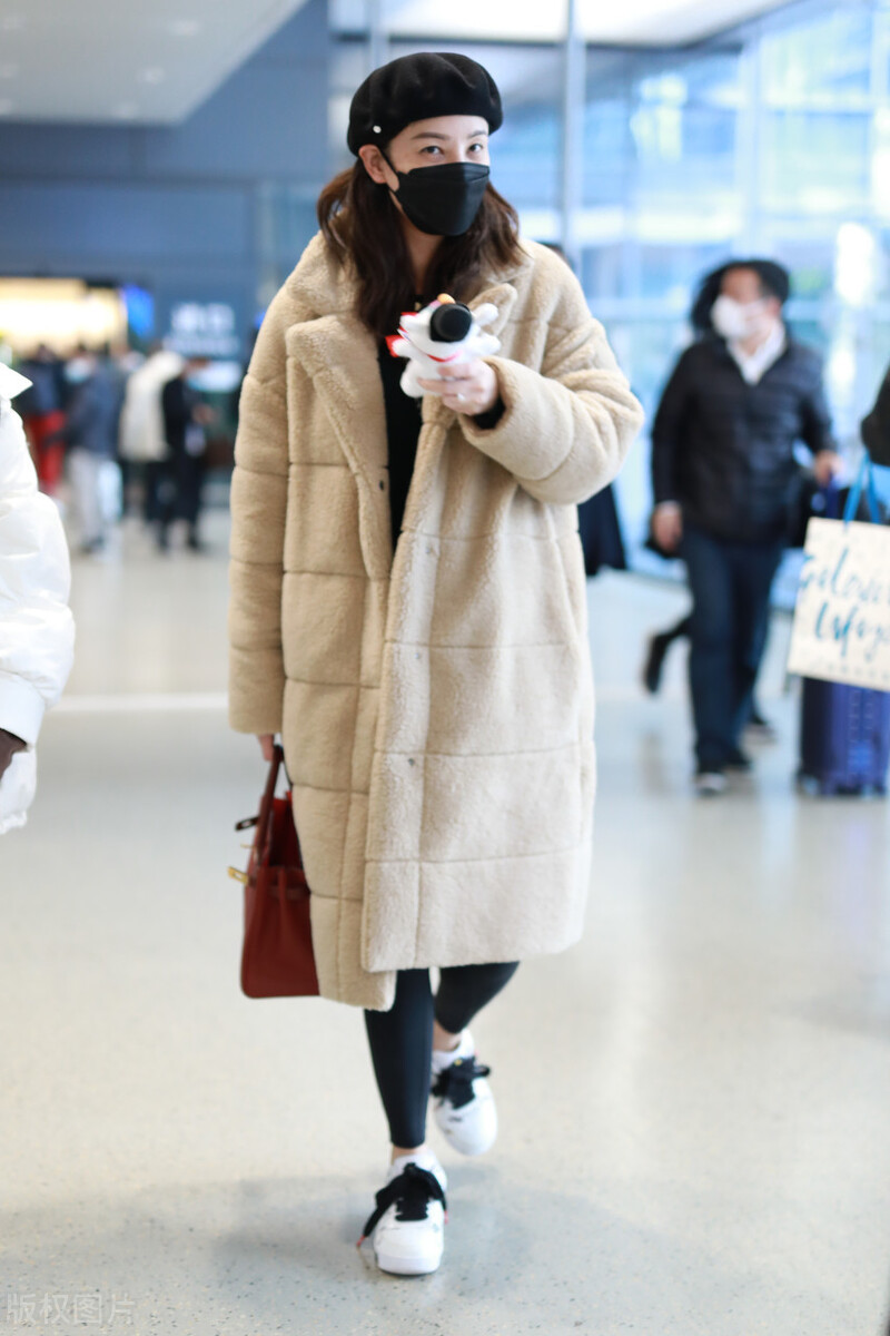 郑希怡穿卡其色羊羔绒大衣现身机场，耳机套当项链精致女孩