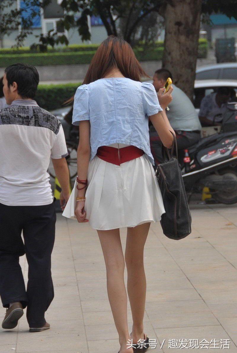 街拍，穿着白色短裙的骨感美女美腿修长，表情纯真笑起来很迷人